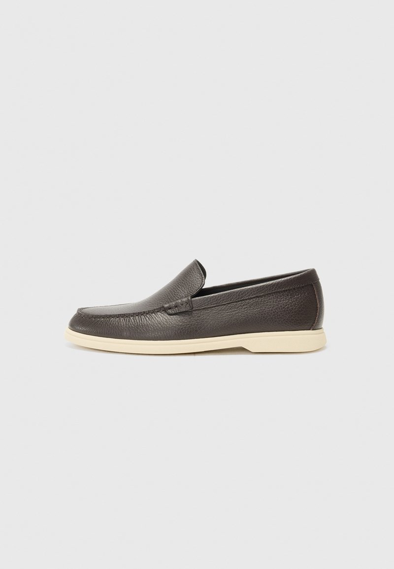 Mocasín de cuero marrón oscuro tipo slip-on con suela de goma blanca y detalles cosidos, mostrado de lado sobre un fondo neutro.