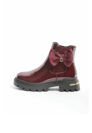 Shiny dark red ankle boot with chunky black sole, side elastic panel, large matching bow, and small gold charm on plain white background.