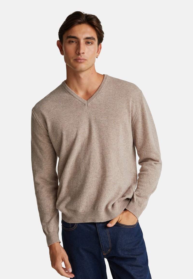 Maglione beige a scollo a V, realizzato in tessuto a maglia, con maniche lunghe e vestibilità rilassata. Indossato con jeans scuri, che mettono in risalto il look informale.