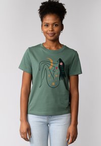 Groene katoenen t-shirt met een grafisch ontwerp van een figuur met sterren, een halve maan en bloemelementen. Korte mouwen en ronde hals.
