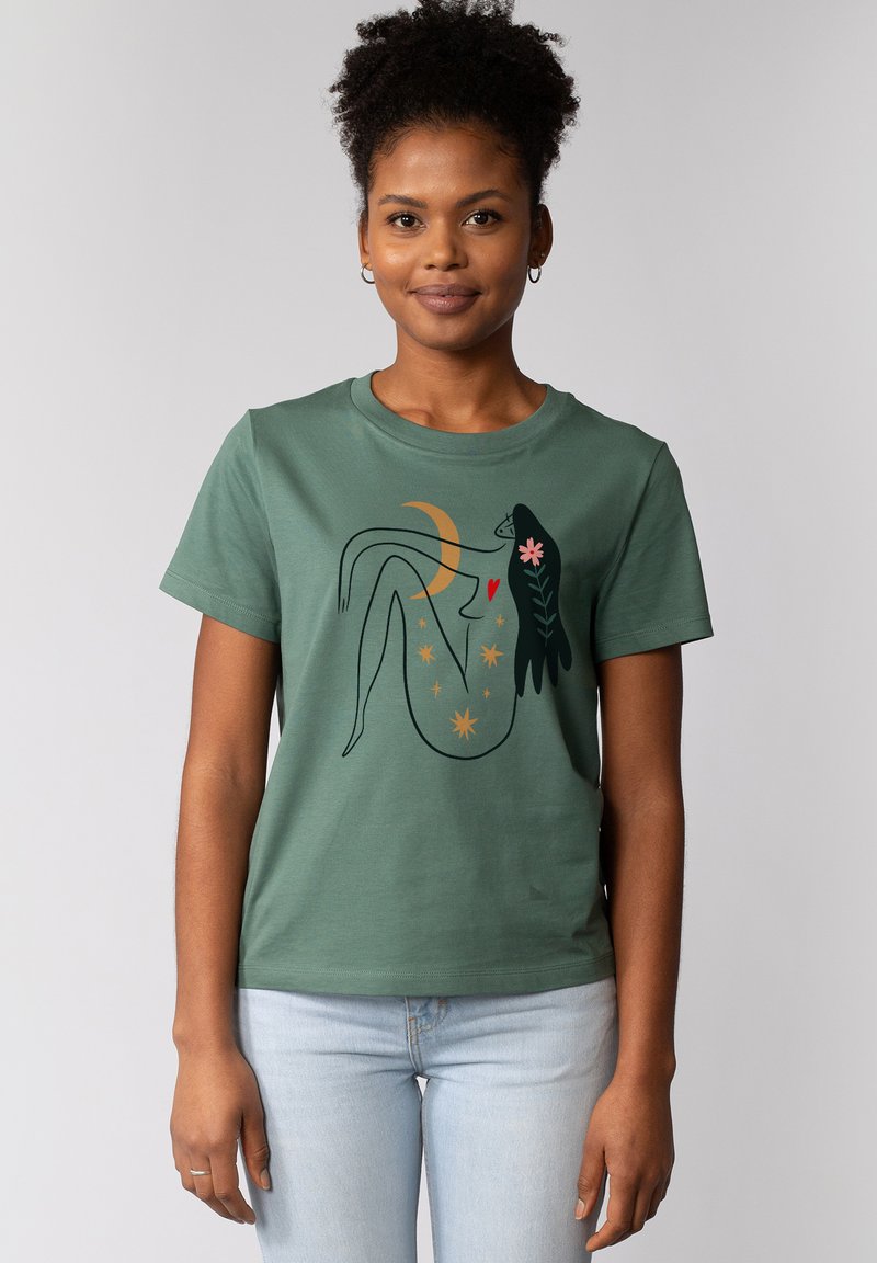 Groene katoenen t-shirt met een grafisch ontwerp van een figuur met sterren, een halve maan en bloemelementen. Korte mouwen en ronde hals.