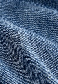Tissu en denim bleu avec un motif de tissage diagonal présenté en gros plan, mettant en valeur la texture et les plis.
