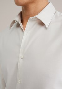 Camisa blanca de vestir con cuello clásico, cierre frontal con botones y textura suave. Presenta costuras en contraste y dos botones en la parte frontal.