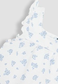 Valge ilma varrukateta kleit, millel on sinine lilleline muster, ripsmetega õlavarre aktsendid ja kogutud vöökoht, et saavutada sobiv välimus.