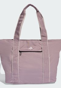 Bolso tote de nylon púrpura con dos asas suaves, un bolsillo delantero con cremallera y un detalle de logo blanco. Presenta bordes contrastantes y una textura suave.