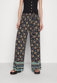 Námořnické kalhoty s širokými nohavicemi a květinovými a paisley vzory v oranžové a tyrkysové barvě. Dokončeno s vzorovaným lemem a volným střihem.
