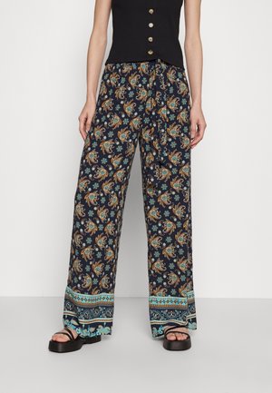 Pantalon large marine avec des motifs floraux et paisley en orange et turquoise. Fini avec des bordures à motifs et une coupe décontractée.