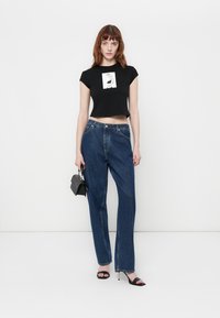 Zwart cropped t-shirt met grafische print, gecombineerd met hoge blauwe denim jeans en zwarte gestrikte sandalen. Kleine zwarte handtas inbegrepen.