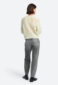 Pull en tricot multicolore pastel avec une coupe ample et un ourlet côtelé, associé à un jean gris taille haute et des chaussures noires.