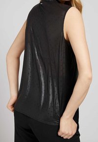 Haut sans manches noir avec une texture lisse, légèrement brillante et un motif de points subtil. Présente un col montant et une coupe décontractée.