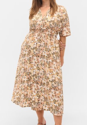 Vrouw draagt een midi-jurk met knopen, korte mouwen, een geel, bruin en roze abstract bloemenpatroon en een getailleerde taille.