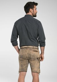 Dunkel gestreiftes Langarmhemd kombiniert mit hellbraunen Ledershorts, die seitliche Schnürungen und Taschendetails aufweisen, getragen von einem Mann von hinten.