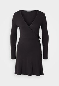 Mustasukainen vaate, joka on valmistettu pehmeästä kankaasta. Siinä on pitkät hihat, V-mallinen kaula-aukko ja vyötärönauha, joka mahdollistaa säädettävän istuvuuden. Helman liehuva muotoilu.