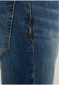 Džíny z denimu ve středně modrém odstínu s oranžovým šitím a černou nášivkou s nápisem "CHASIN'" na levé straně. Slim fit s klasickým designem.