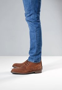 Bruine leren enkellaarzen met een gestructureerde afwerking, voorzien van veters en een rubberen zool, gecombineerd met blauwe slim-fit jeans.