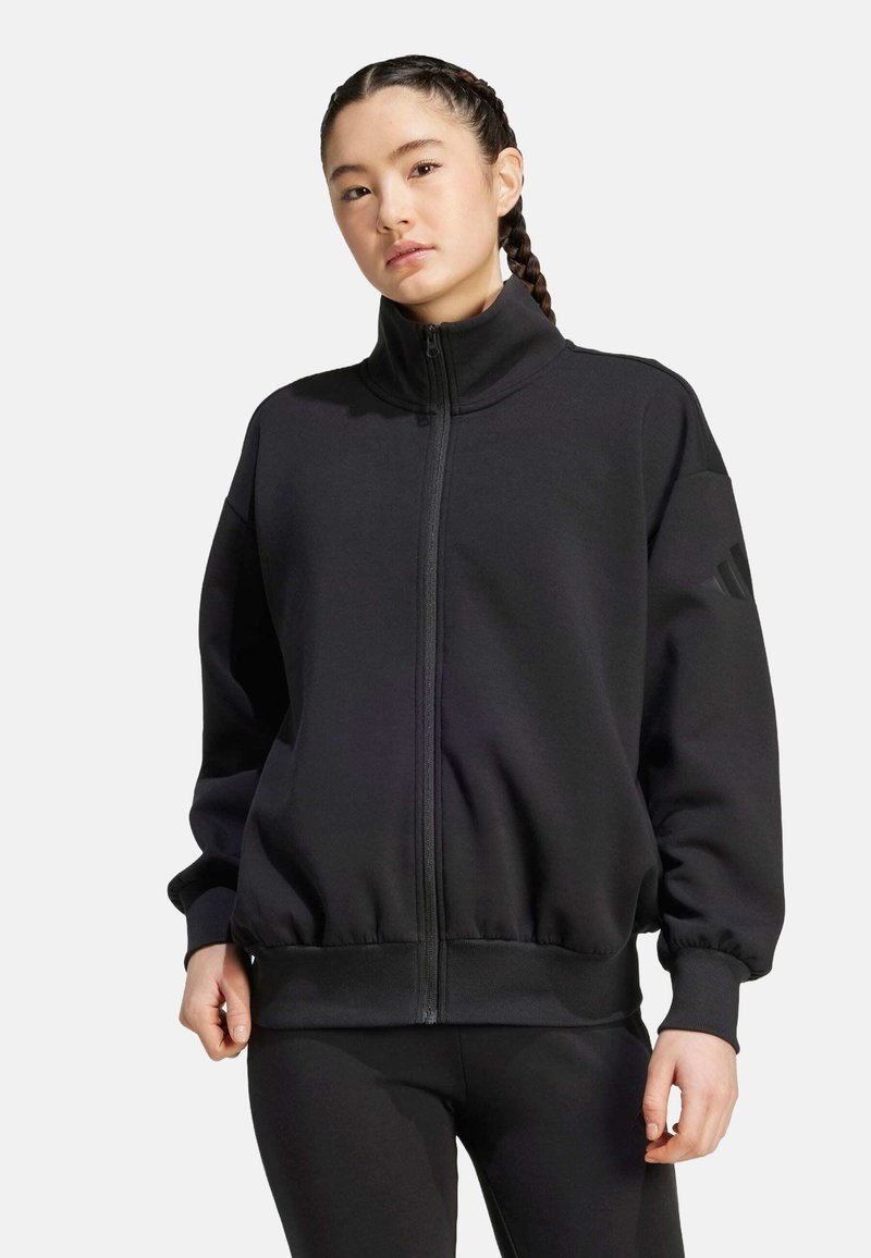 Black zip-up sweatshirt with high collar, ribbed cuffs and hem, featuring a logo accent on the sleeve, made from soft textured fabric.