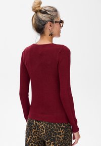 Czerwony sweter dopasowany, o prążkowanej fakturze, z okrągłym dekoltem i długimi rękawami, zestawiony z spodniami w cętkowany wzór w panterę dla kontrastu.