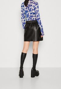 Pitkähihaisen sinivalkoraidallisen paidan yhdistelmä mustan nahkaisen minihameen kanssa. Mukana korkeavyötäröinen malli ja polven ylle ulottuvat mustat nahkaiset korkeat saappaat.