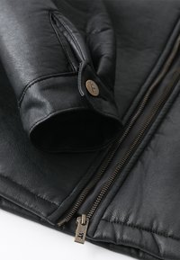 Black leather jacket featuring a zippered front, quilted texture on sleeves, and a round button accent on the cuff.