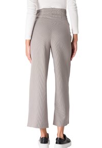 Pantalons taille haute, à jambes larges, dans un motif pied-de-poule marron et beige. Présentent une texture lisse et un ourlet soigné. Portés avec des chaussures noires.