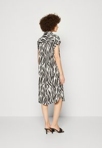 Fekete-fehér zebra mintás ruha rövid ujjakkal, galléros nyakkal és oldalsó hasítékkal; sima anyag és térd fölé érő kialakítás.