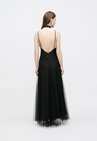 Black gown with a low v-back, thin straps, and layered tulle skirt. Features a fitted bodice and textured lace accents at the hem.