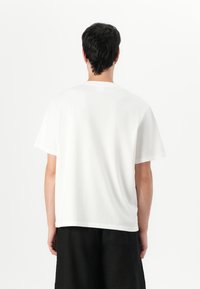Hvit bomulls T-skjorte med kort erm og løs passform. Bakvinduet viser en rund hals og jevn tekstur, kombinert med svarte shorts.