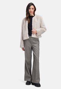 Kunstpels cropped jakke i lys beige, med rund halsudskæring og åben front. Stylet med grå flagrende bukser og sorte platform sko.