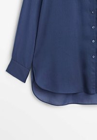 Chemise bleu marine à manches longues avec boutons, manches retroussées et ourlet courbé sur fond blanc.