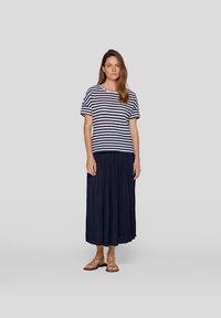 Striped short-sleeve top in navy and white, paired with a long navy pleated skirt. Worn with flat brown sandals, displaying a relaxed silhouette.