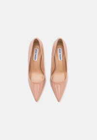 Pump con tacco alto in vernice color nude, con punta affusolata e una finitura liscia e lucida. Presenta un'etichetta interna con "Steve Madden."