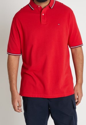 Rød polo shirt med en blød tekstur, der har en klassisk krave, to-knaps placket og kontrasterende navy- og hvide stribede detaljer på kraven og ærmerne.