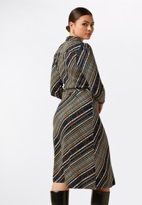 Långärmad klänning i mörkt tyg med flerfärgade geometriska mönster, åtsittande vid midjan, med krage och midi-längd.