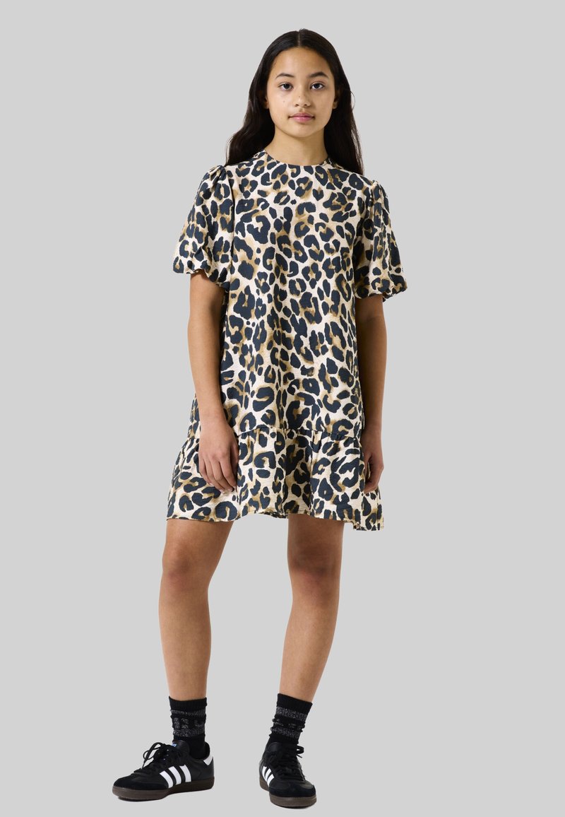 Vestido de estampado de leopardo con mangas cortas abullonadas, forma fluida y dobladillo en capas. Llevado con zapatos negros y calcetas con estampado.