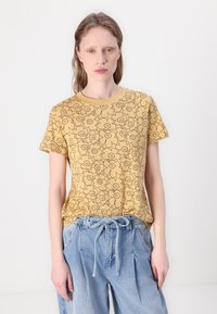 Yellow cotton t-shirt with black floral print, round neckline, and short sleeves. Paired with light blue, loose-fitting denim trousers.