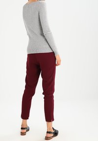 Maglione grigio a coste con maniche lunghe abbinato a pantaloni bordeaux a sigaretta. Sandali neri con dettaglio a fibbia completano l'outfit.