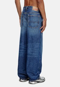 Jeans en denim bleu à jambes évasées avec une finition délavée, présentant une étiquette en cuir au dos de la taille et deux poches arrière.