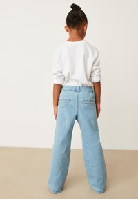 Jeans din denim de culoare albastră deschisă, cu o croială confortabilă, având două buzunare spate și manșete răsucite. Asortate cu o cămașă albă cu mânecă lungă.
