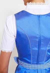 Blå klänning med prickmönster, hög hals och spetsdetaljer. Baksidan har en dragkedjestängning och ett rutigt midjeband.