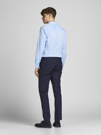 Light blue long-sleeve shirt with buttoned cuffs, paired with dark plaid trousers and black suede shoes. Simple, tailored fit design.