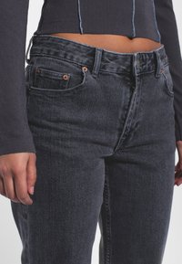 Jeans in denim nero a vita alta, con rivetti in rame, zip sul davanti e orlo leggermente sfilacciato in vita. Tessuto con texture visibile.