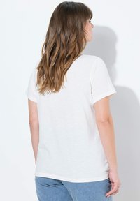 Camiseta de algodón blanca con mangas cortas enrolladas y un ajuste relajado, que presenta una textura suave y un dobladillo recto, vista desde la parte de atrás.