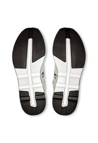 Black and white running shoe soles featuring a textured rubber surface, defined grooves, and logo. Durable material with contrasting color accents.