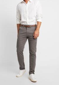 Grijze, slim-fit broek gemaakt van een katoenmix. Heeft een klassiek vijf-pocket ontwerp, gecombineerd met een bruine leren riem en witte sneakers.