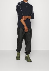 Suéter azul marino con detalles en blanco, pantalones ligeros negros y zapatillas deportivas verdes. Cuenta con un cuello redondo y un corte relajado.