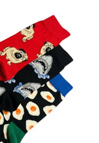 Trois chaussettes colorées avec des motifs distincts : rouge avec des carlins, noire avec des requins, et noire avec des œufs au plat et des poignets bleus.