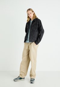 Black denim jacket, light blue t-shirt, beige wide-leg trousers, and gray sneakers with dark accents. Simple, casual outfit.