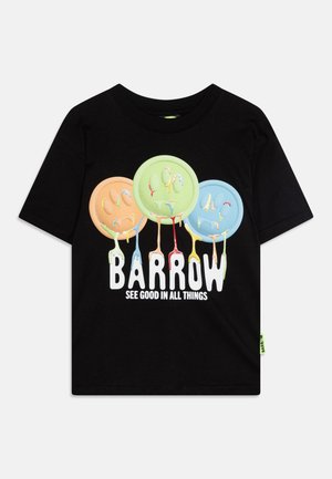 T-shirt en coton noir avec trois visages souriants colorés en orange, vert et bleu, avec des détails de peinture qui coule et un texte blanc en gras en dessous.