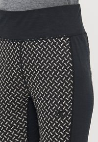 Fekete sport leggings, textúrált zikk-zakk mintával, széles derékpánttal és logó részlettel az oldalon.