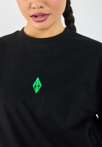 Svart bomull T-skjorte med rund hals og en grønn diamantformet logo på brystet, med en strukturert overflate.